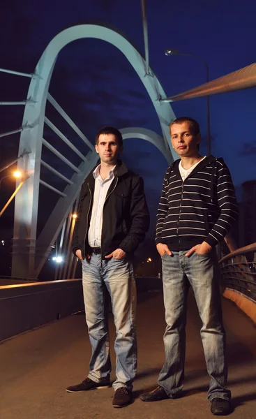 Two guys standing on the night bridge and looking at camera — Stock Photo, Image