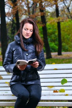 Beautiful woman is sitiing in park and reading clipart