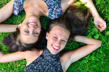 İki bayan arkadaş çimenlerde uzanıyor ve gülüyor.