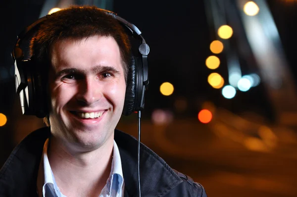 Smiling man is listening music at city night street — Stock Photo, Image