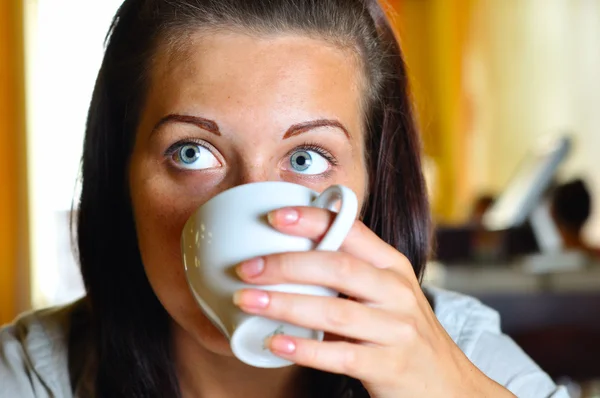 Mujer joven está tomando café en la cafetería y mirando hacia los lados — Foto de Stock
