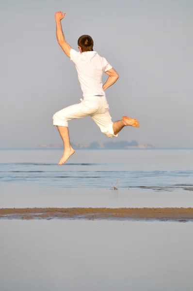 Człowiek w białej sukni jest skakanie na plaży rano — Zdjęcie stockowe