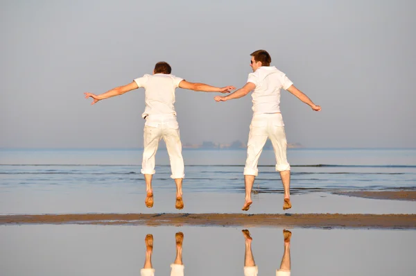 Двоє друзів стрибають на ранковому пляжі — стокове фото