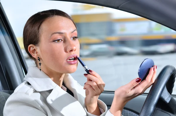 Mujer elegante está haciendo maquillaje en la carrera en su coche — Foto de Stock
