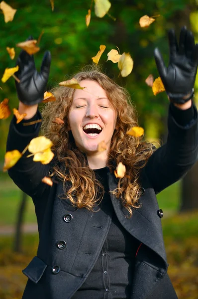 Šťastná žena je házení suché podzimní listí v parku — Stock fotografie