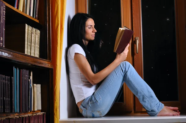 Mooie vrouw zit op venster en leesboek — Stockfoto