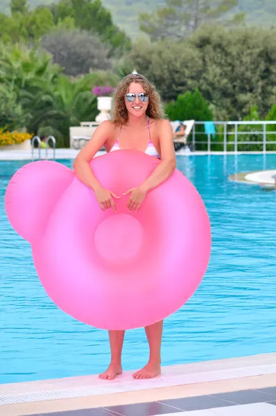 Mujer divertida está sosteniendo una cama de aire redonda rosa en las manos cerca de la piscina — Foto de Stock