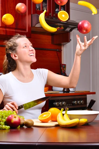 Happy woman is cooking fruit salad out of flying fruits — Stock Photo, Image