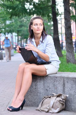 Beautiful woman is sitting in an alley with laptop and looking s clipart