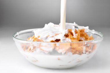 Milk stream flowing to the bowl with corn flakes clipart