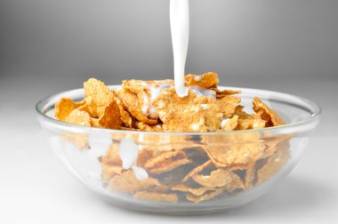 Milk stream flowing to the bowl with corn flakes clipart