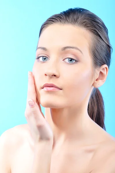 Beautiful woman is touching her face, on blue background — Stock Photo, Image