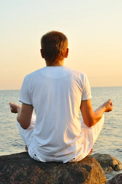 年轻男子坐在一块石头上，看看海上日出。视图 — 图库照片