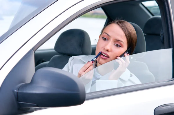 Elegant woman is doing makeup and talking phone on the run in he — Stock Photo, Image