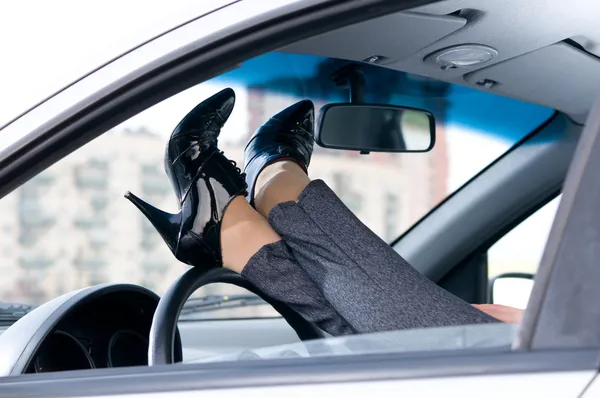 Slim female legs are lying on steering wheel — Stock Photo, Image