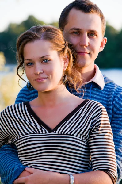 Young attractive couple near lake at sunset — Stockfoto