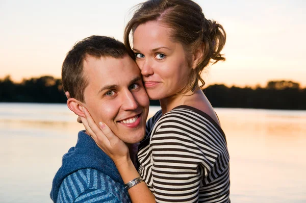Young attractive couple near lake at sunset — Stock Photo, Image