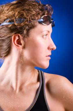 Pretty woman swimmer is looking sideways on blue background