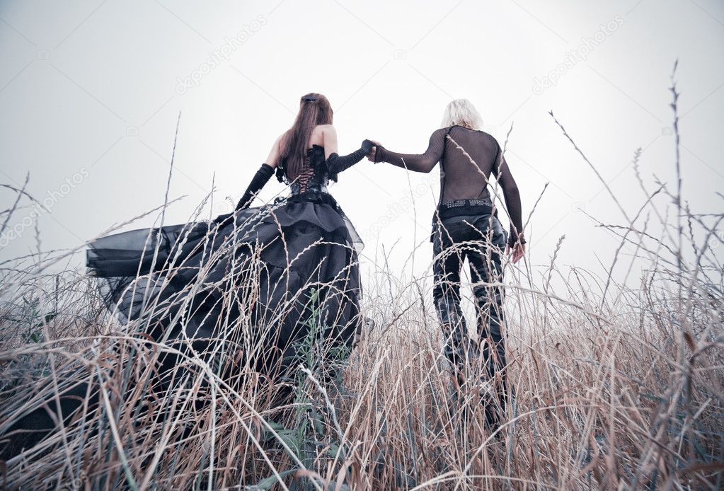 Young goth couple walking on field. Bright white colors.