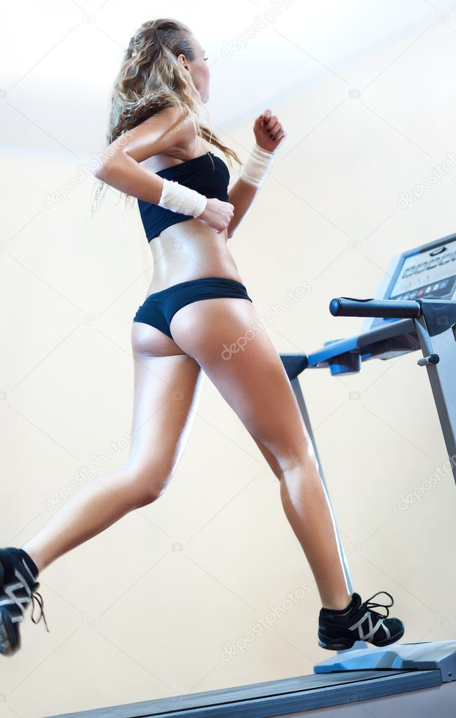 Young woman running on treadmill in gym.