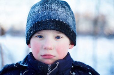 The sad crying boy with blue eyes in winter clothes clipart