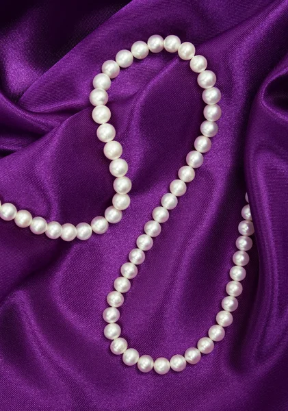 Perle bianche su una seta lilla — Foto Stock