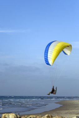 Paramotor, a motorized paraglider, flying above the beach of Mediterranean sea clipart