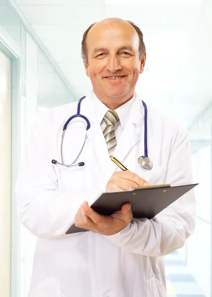 Feliz sonriente médico maduro escribiendo en el portapapeles en un hospital moderno — Foto de Stock