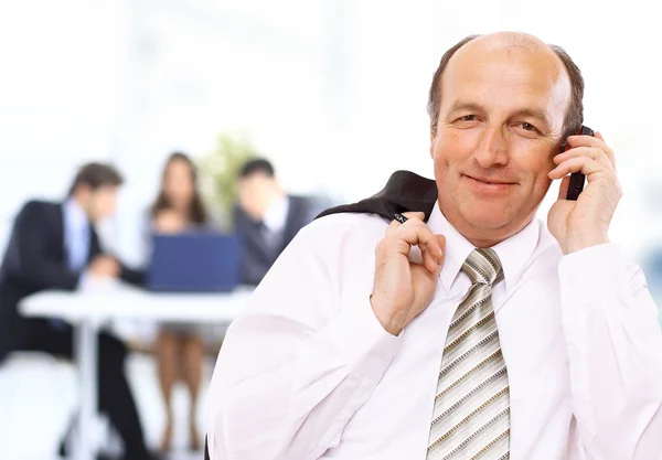 Улыбающийся бизнесмен, использующий мобильный телефон с коллегами на размытом фоне — стоковое фото