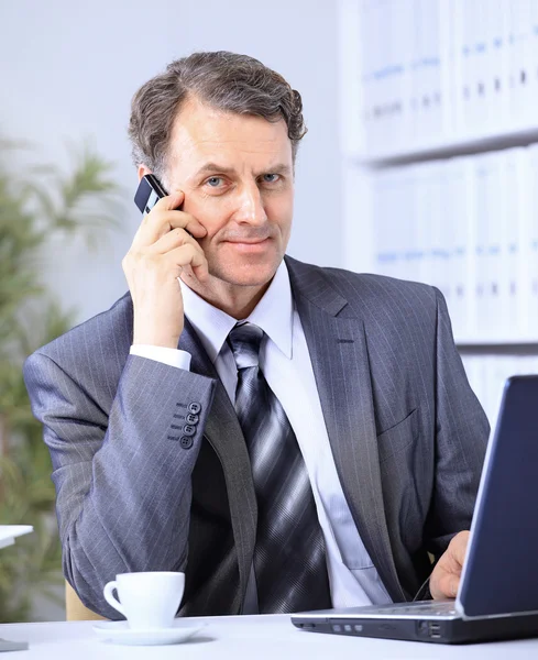 Бизнесмен, сидящий в офисе с ноутбуком по телефону — стоковое фото
