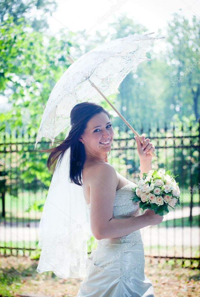 Bride portrait with lacy umbrella in sunny park