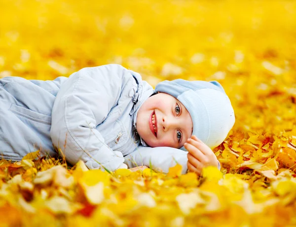 Kleine jongen liggend op de gele bladeren — Stockfoto
