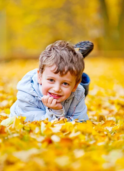 Küçük çocuk yalan sarı yapraklarda — Stok fotoğraf