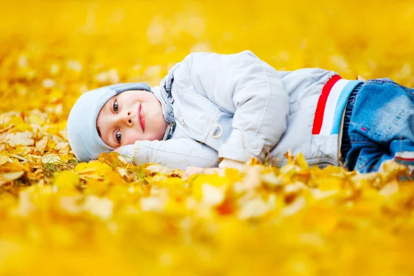 Menino deitado nas folhas amarelas — Fotografia de Stock