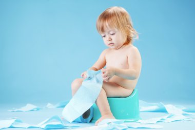 Studio shot of funny toddler sitting on potty chair and playing with toilet paper clipart