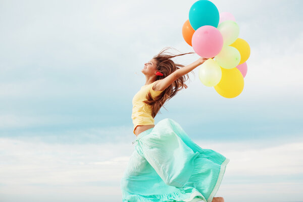 Счастливая девушка с кучей разноцветных воздушных шаров на пляже
