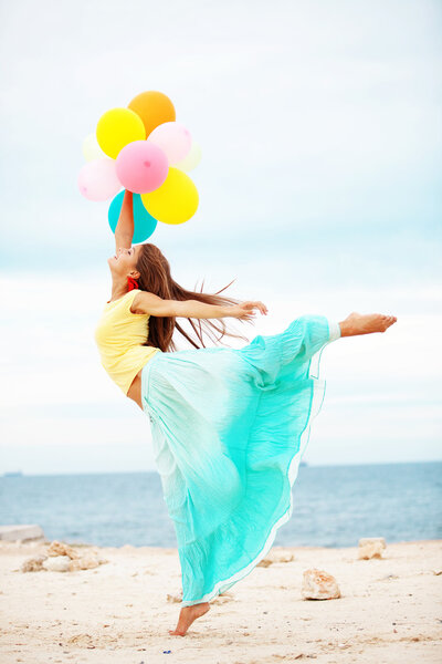 Счастливая девушка с кучей разноцветных воздушных шаров на пляже

