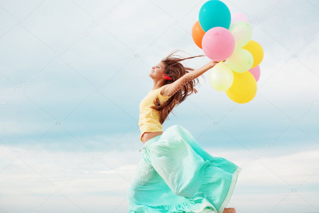 Happy girl holding bunch of colorful air balloons at the beach