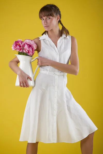 黄色の背景上に花の花瓶を置く女性 — ストック写真