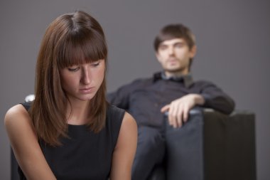 Couple problem - sad woman sitting in foreground, man in background clipart