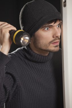 Burglar with pocket lamp looking into the room clipart