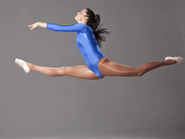 Kobieta Gimnastyk Robi Dzieli Się Powietrzu Nad Szarym Tle — Zdjęcie stockowe