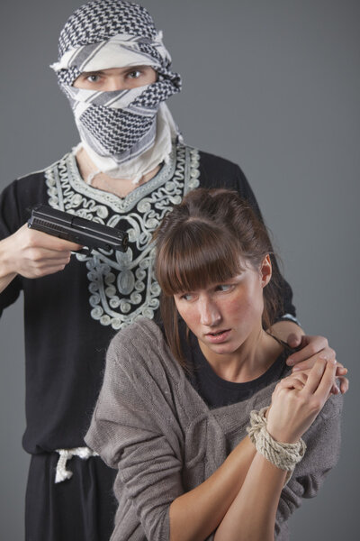 Female hostage and hijacker with gun over grey background