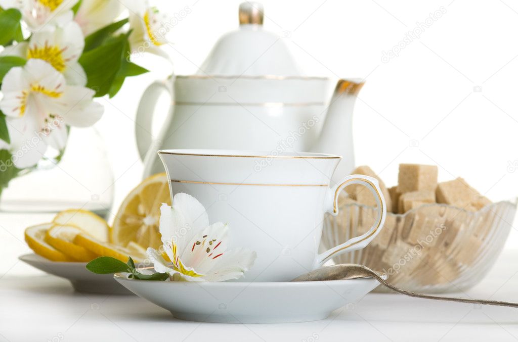 Cup of tea and teapot on table with flowers isolated over white