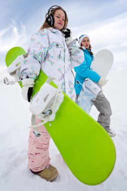 Girl in phones with green snowboard and her friend in blue in mouintains clipart