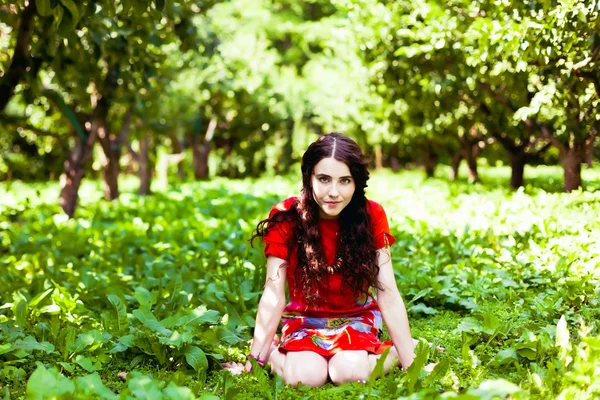 Dziewczynka w czerwonej sukience siedzenia w trawie — Zdjęcie stockowe