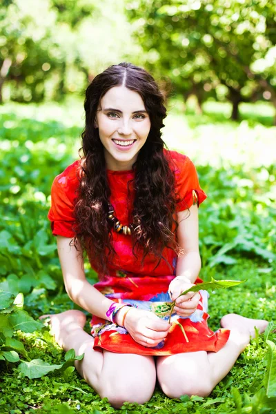 Девушка в красном платье сидит в траве и улыбается — стоковое фото