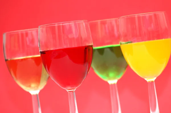 赤の背景に様々 な色の飲み物とメガネ — ストック写真