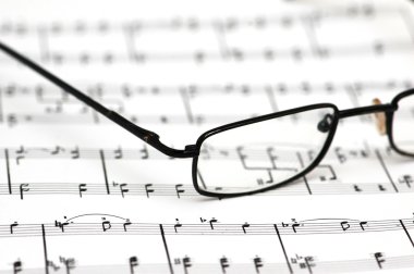 Black reading glasses over the music sheets clipart