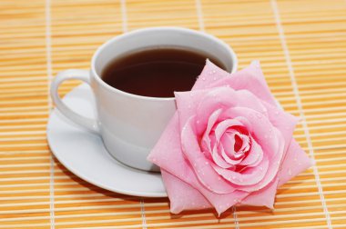 Cup of black tea and rose on orange mat clipart